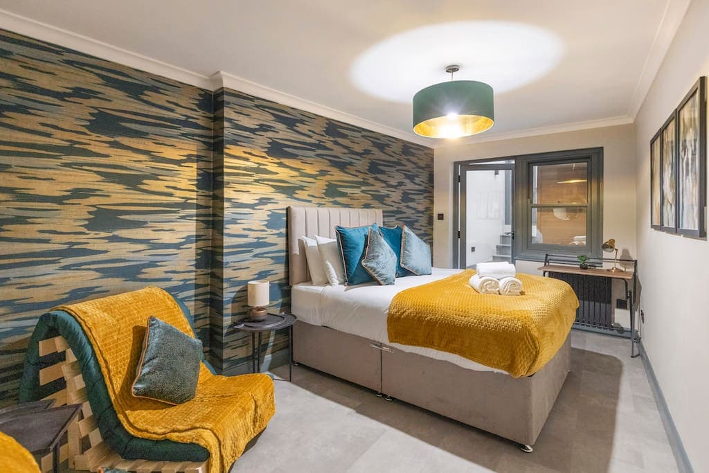 Relax in the stylish Modern & Funky Games Room & Sauna bedroom, featuring two cozy armchairs for lounging and a sleek desk, perfect for work or unwinding in this unique and vibrant retreat.