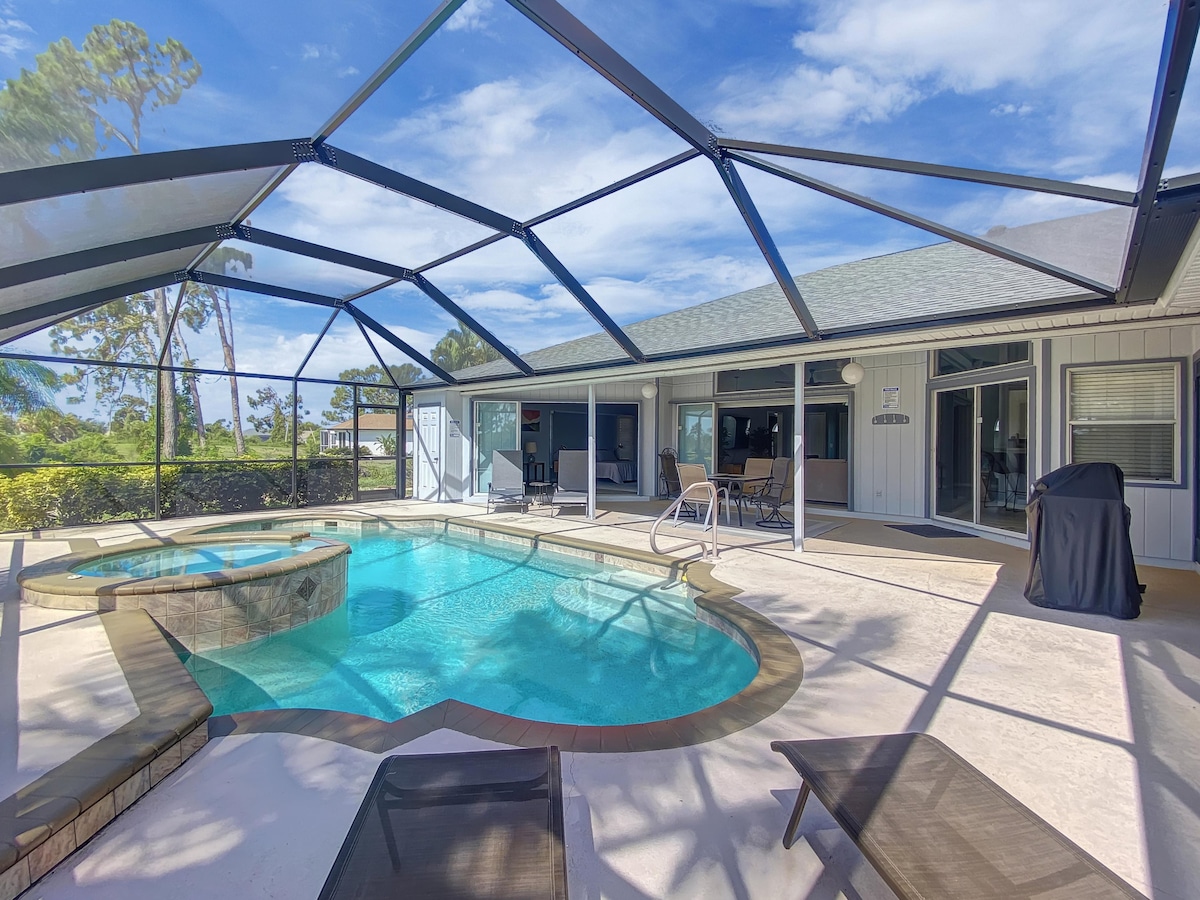 A screened lanai is depicted featuring a heated pool and spa, surrounded by lounge chairs. Direct views of the outdoors are enhanced by the clear blue sky. Notable is the outdoor dining area, accompanied by a BBQ grill, providing an inviting space for relaxation.