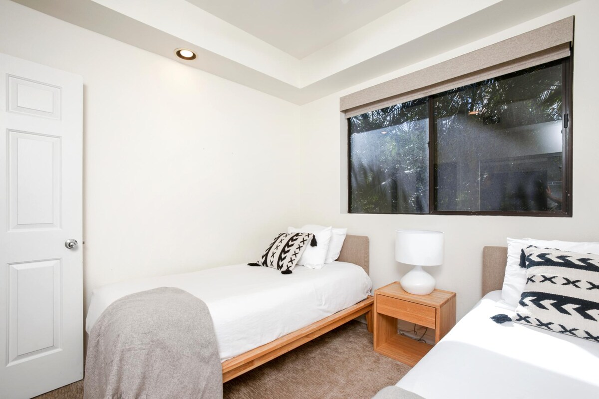 Jednostavno utočište s dvostrukim krevetima, udobnim pokrivačima i sunčevom svjetlošću koja se probija kroz mirne zelene poglede