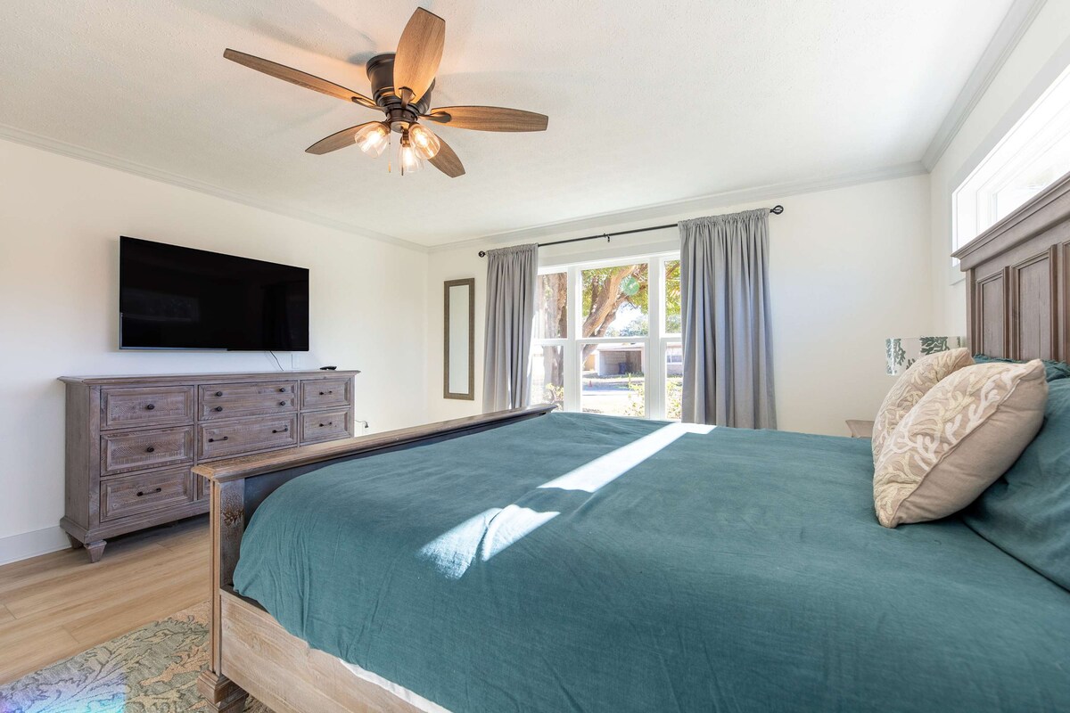 غرفة نوم رئيسية واسعة بسرير كبير الحجم وأثاث خشبي أنيق ونوافذ كبيرة تملأ الغرفة بالضوء. ملاذ مثالي للنوم المريح.