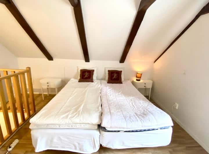 המיטה ממוקמת בקומה העליונה; החדר מואר ומאוורר עם תקרה גבוהה וקורות עץ בתקרה.