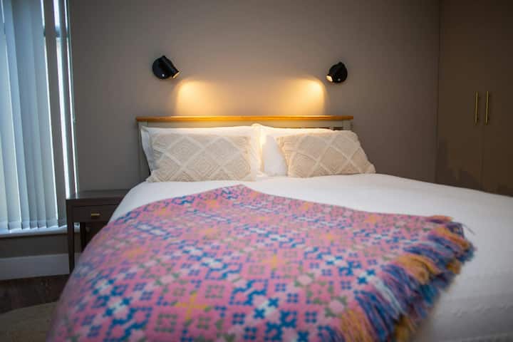 King size bed  with wall lights above the bed, bed side table and Welsh blanket on bed