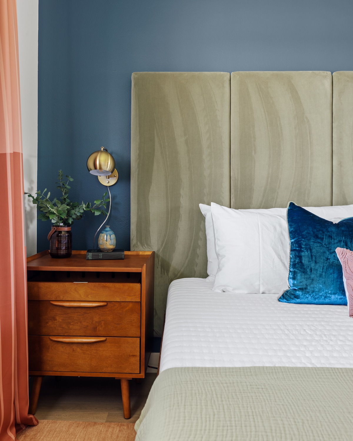 Modern retreat with velvet headboard, mid-century nightstand, and cozy bedding.