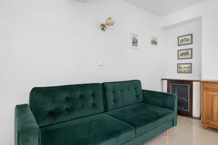 Acogedor dormitorio con un sofá verde y obras de arte enmarcadas.