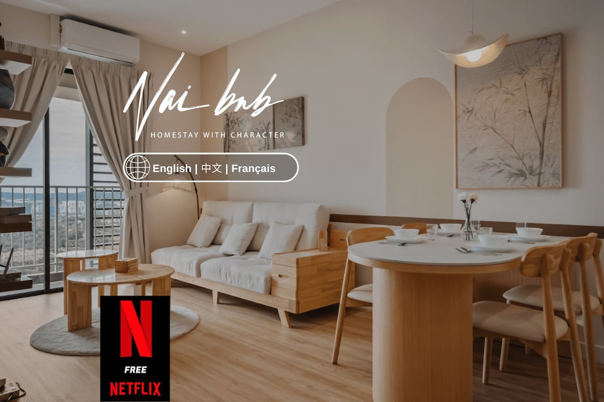 The living area features a light color palette with wooden accents. A large window allows natural light to fill the space, which includes a cozy sofa and a dining table. A minimalist pendant light hangs above the table, enhancing the room's serene atmosphere.