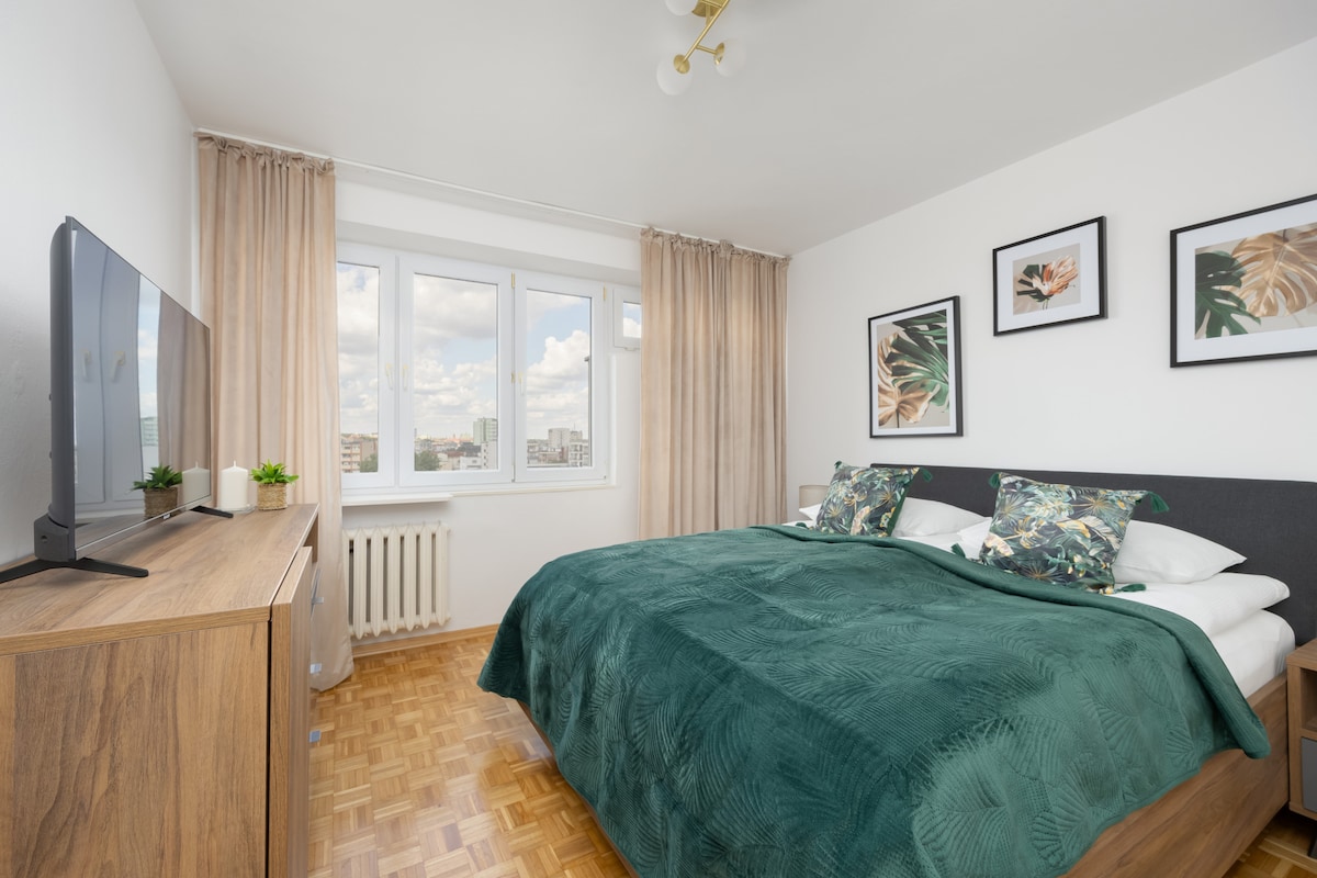 Un dormitorio cómodo con una cama doble, suelos de madera y ventanas grandes. Una suave colcha verde aporta un toque de calma a un espacio luminoso.