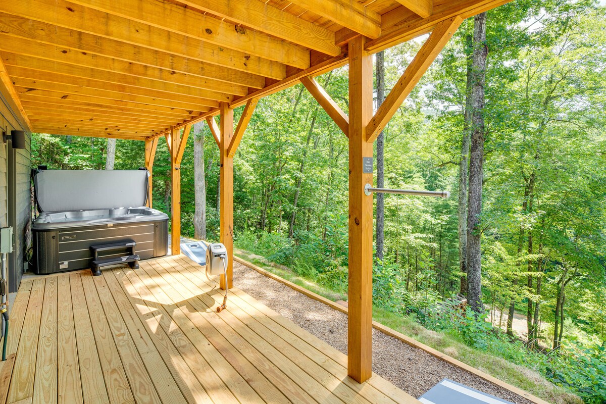 An outdoor deck features natural wood finishes, providing an inviting space to relax. A private hot tub is situated near the edge, surrounded by a serene wooded landscape. The area includes ample space for seating and enjoying nature.