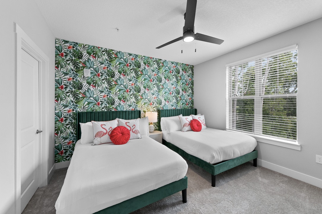 客房设有两张单人床，配有白色床上用品和明亮的粉色抱枕，与整体热带主题相匹配。 床上有深绿色的天鹅绒床头板。