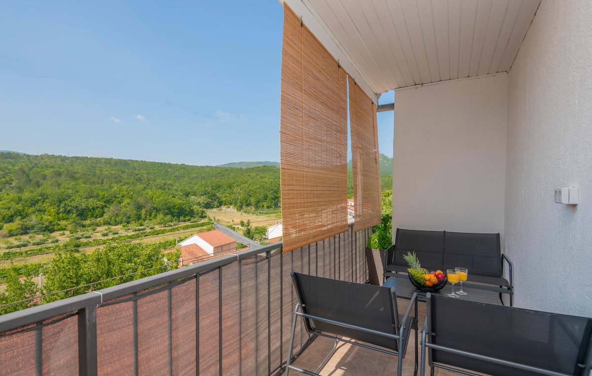 A private balcony features a seating area with black chairs and a small table. Scenic views of lush greenery extend into the distance, while sun shades provide a comfortable space to enjoy refreshments, making it an ideal spot for relaxation.