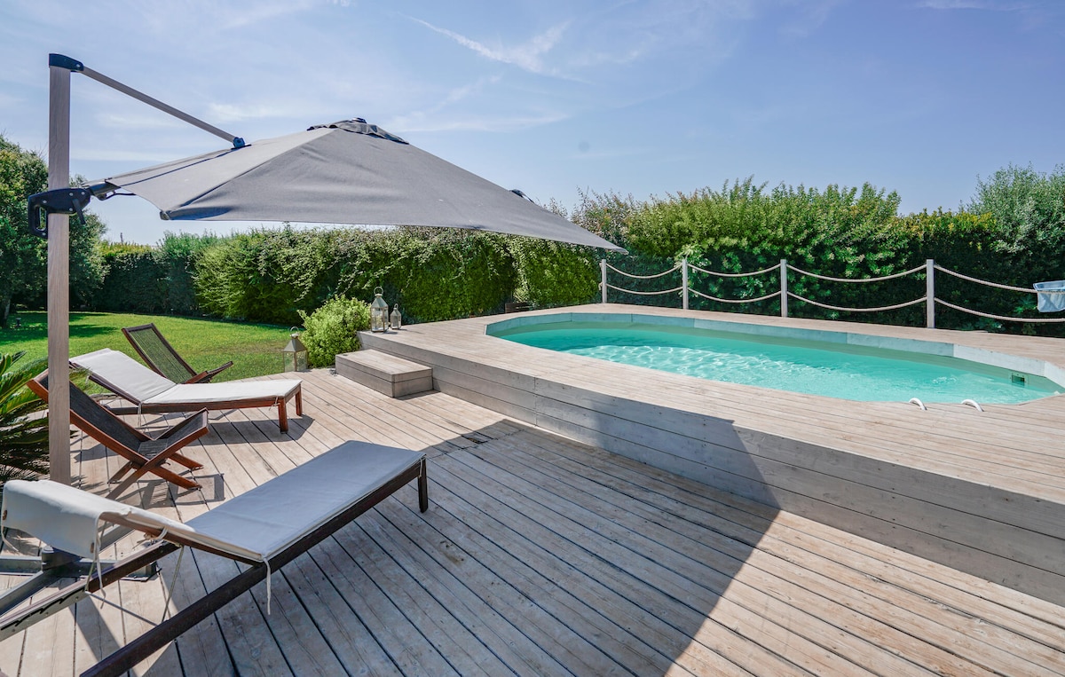 A private swimming pool is set within a wooden deck, accompanied by two loungers positioned for relaxation. A large shade umbrella provides coverage, while a lush green hedge frames the area, contributing to a sense of privacy in this tranquil outdoor space.