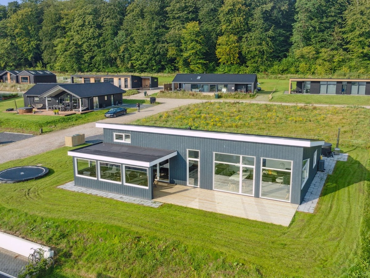 A modern single-family house is surrounded by a well-kept garden and grassy areas. Large windows allow natural light to fill the interior, and a spacious terrace extends from the building. A trampoline is visible in the yard, along with other nearby structures.