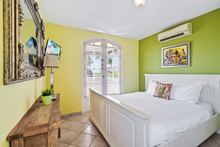 - בחדר השינה יש מיטת קינג סייז נוחה עם מצעים לבנים חדים וכרית דקורטיבית
- קירות צהובים וירוקים בהירים מוסיפים אווירה עליזה ותוססת לחלל
- דלתות מאפשרות לאור טבעי להציף את החדר, ומשפרות את התחושה האוורירית שלו