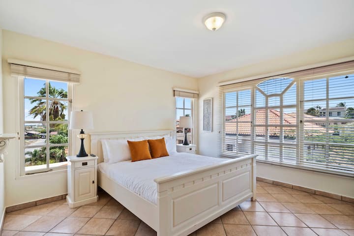 - מיטת קינג סייז עם מצעים לבנים חדים וכריות נוי כתומות תוססות
- החלונות מספקים הרבה אור טבעי ומציעים נופים מרהיבים של האזור שמסביב
- החדר מקושט בשידות ליד המיטה, ומנורות למראה אלגנטי