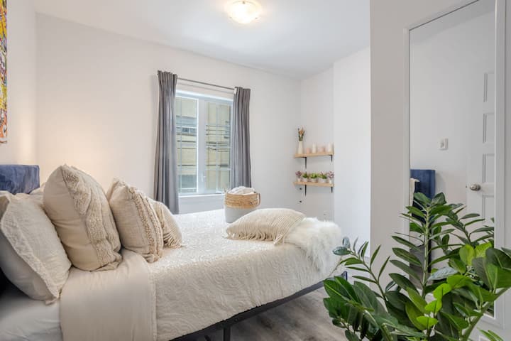 Bedroom 2: Spacious second bedroom with plush bedding, blackout curtains, and lush greenery for a fresh vibe