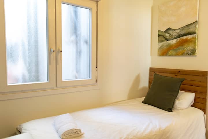 Ova fotografija ističe sekundarnu spavaću sobu koja odiše jednostavnošću i udobnošću. Krevet za jednu osobu uredno je namješten od hrskave bijele posteljine i zemljanog zelenog ukrasnog jastuka koji se lijepo spaja s obližnjim obojenim zidom.