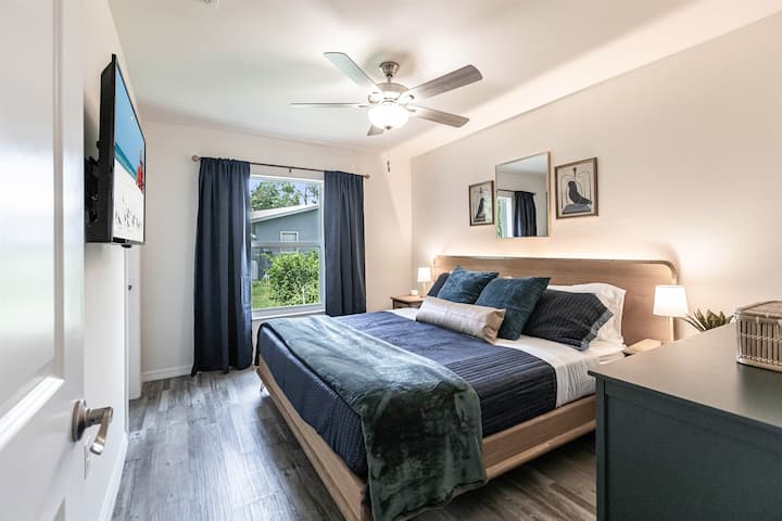 Unidad 1978: acogedor dormitorio con una cama tamaño king, sábanas y detalles vibrantes. Una gran ventana con cortinas, un ventilador de techo y una decoración moderna crean un refugio relajante.