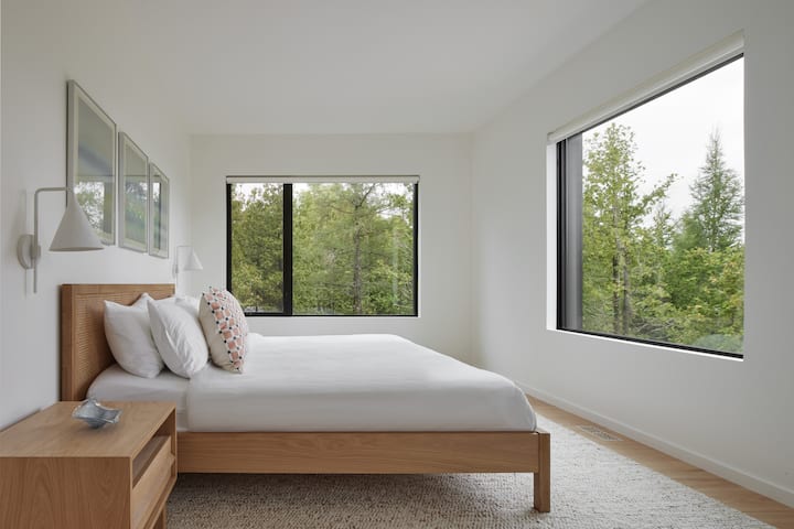 Dormitorio 1: Un dormitorio minimalista con grandes ventanales que ofrece vistas apacibles a la vegetación circundante.