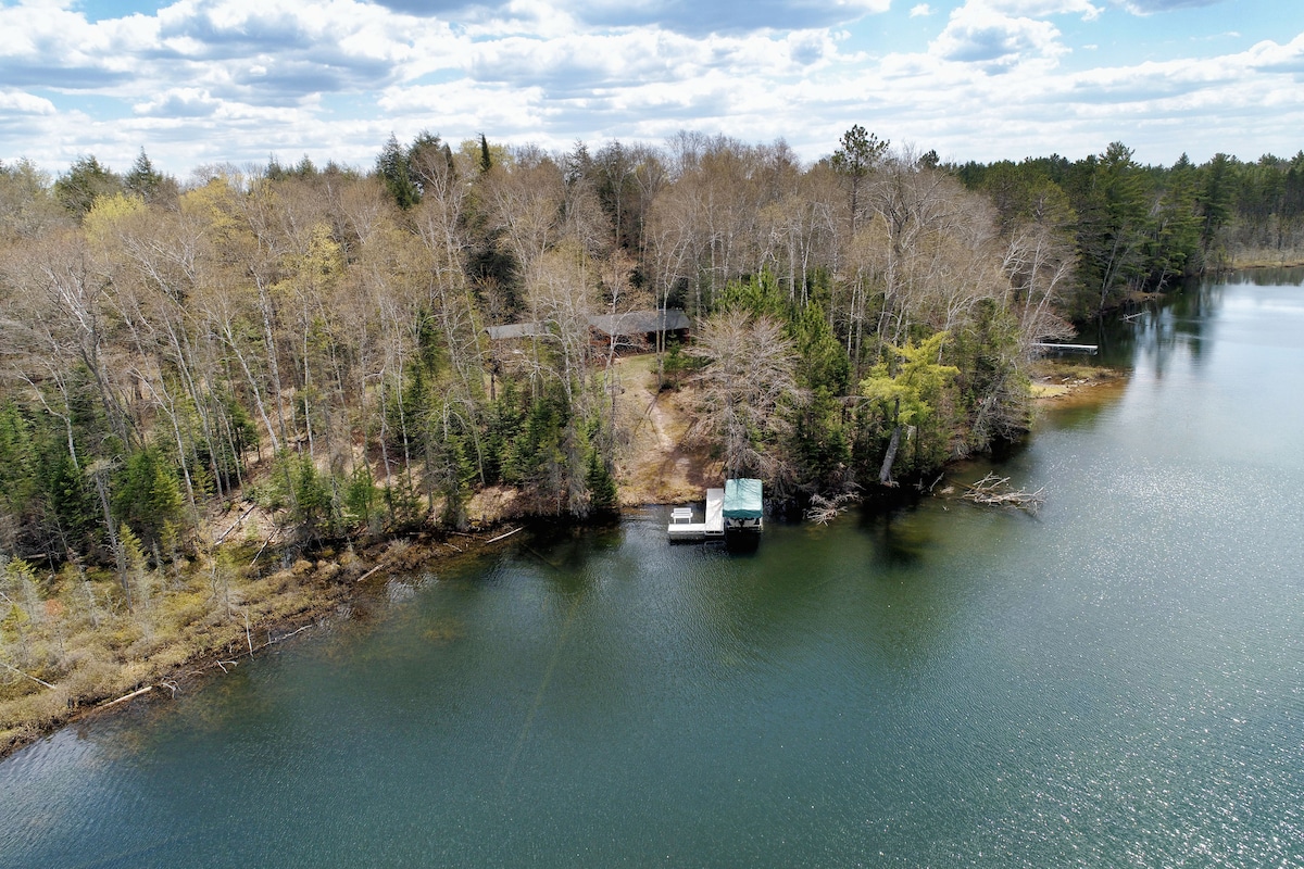 The lakeside property is framed by mature trees, creating a natural boundary. The dock extends into the calm waters of Buffalo Lake, providing access for boating. Surrounding terrain showcases varied vegetation, reflecting the essence of the Northwoods landscape.