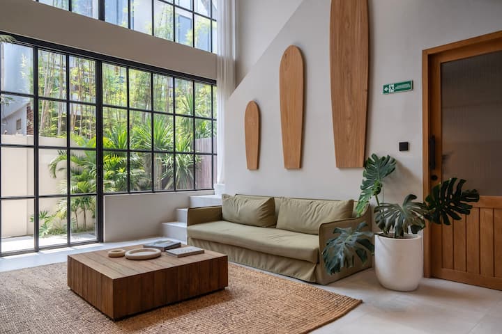 แสงแดดสาดส่องเข้ามาในห้องนั่งเล่นที่มีสไตล์ด้วยเพดานสูงวิวสวนที่เขียวชอุ่มและการเน้นไม้ธรรมชาติที่สร้างบรรยากาศที่อบอุ่นและน่าอยู่