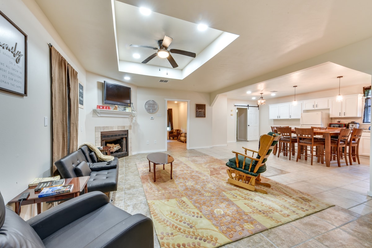 A spacious living area features a fireplace, comfortable seating, and a decorative rug with intricate patterns. Bright overhead lighting enhances the open layout that integrates with a dining space equipped with a large table and multiple chairs.