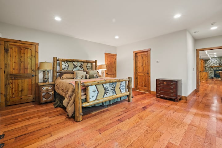 Chumba cha kulala chenye nafasi kubwa kilicho na fremu ya kitanda ya mbao ya kijijini iliyo na matandiko yaliyohamasishwa na mazingira ya asili, sakafu ngumu za mbao na mbao zenye joto. Mapumziko haya yenye starehe hutoa sehemu yenye utulivu na starehe ya kupumzika.