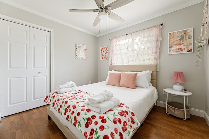 Chambre joyeuse avec literie florale, ventilateur de plafond et lumière vive de la fenêtre.