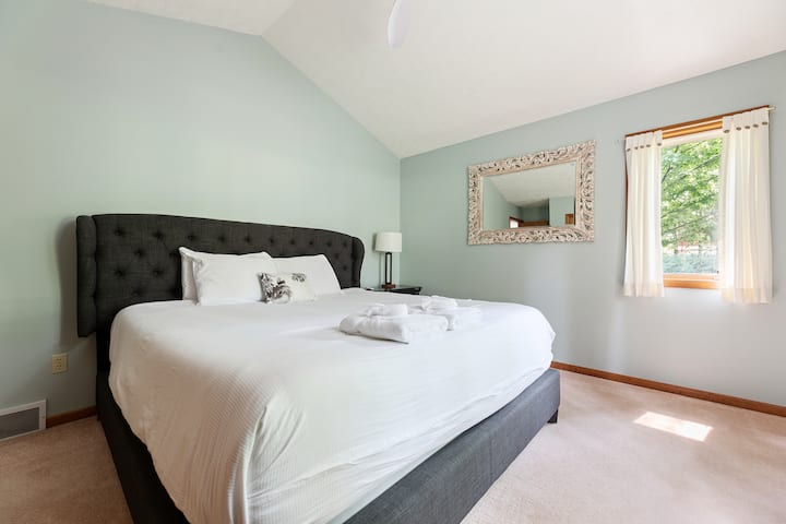 Ოთახი გაფორმებულია რბილი პასტელური კედლებით, საწოლის ზემოთ დიდი დეკორატიული სარკით და ბუნებრივი სინათლით, რომელიც ჩნდება მსუბუქი ფარდებით გამოწყობილი ფანჯრიდან, რაც ქმნის მშვიდ და მიმზიდველ ატმოსფეროს.