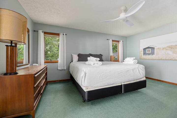 Ნათელი და ჰაეროვანი საძინებელი დიდი ზომის საწოლით, ღია ცისფერი კედლებითა და მწვანე ხალიჩით.