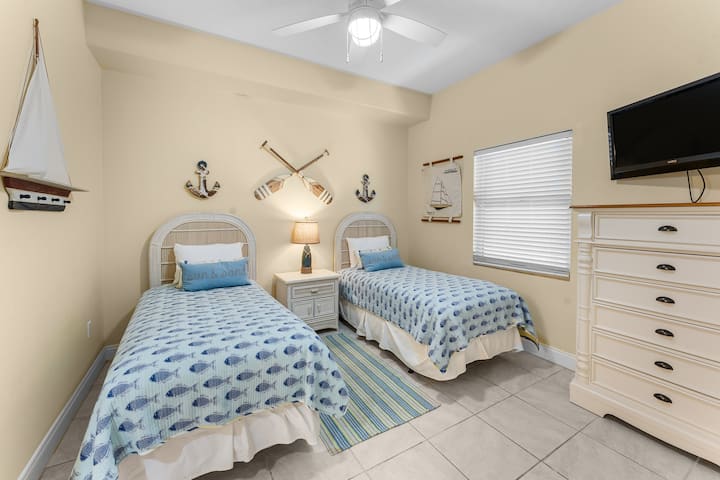 Quarto aconchegante com duas camas individuais, decoração náutica e luz natural.