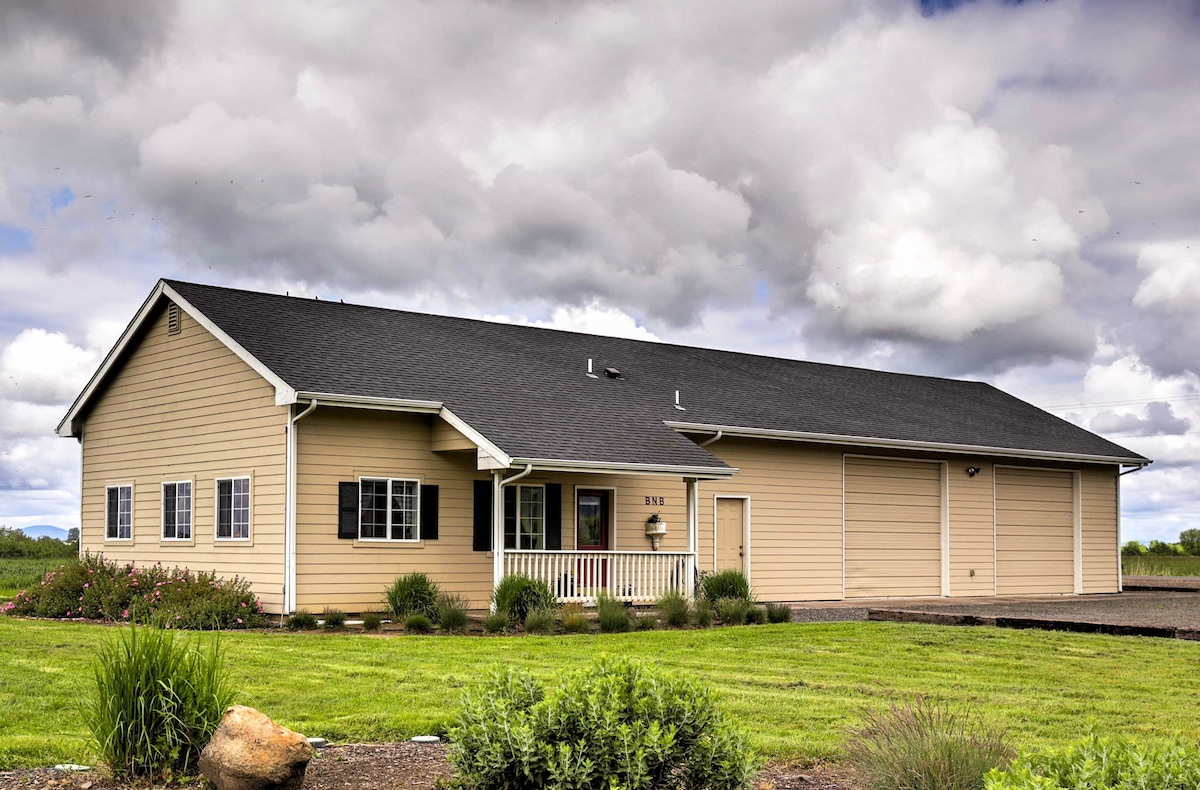 The exterior of the property features a single-story house with light-colored siding and a black roof. A small porch is positioned at the front, framed by neatly landscaped greenery. The expansive lawn is bordered by flowering plants, creating a welcoming entrance.