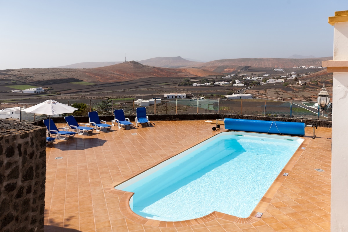A private outdoor pool is surrounded by sun loungers, inviting relaxation under the sun. Expansive views of the valley and distant hills are visible, providing a serene backdrop. An umbrella offers shade beside the pool, enhancing the outdoor space.