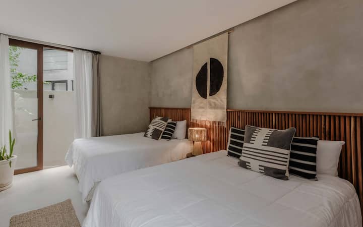 Another comfortable bedroom with two queen beds with a circular mirror and warm wood tones.