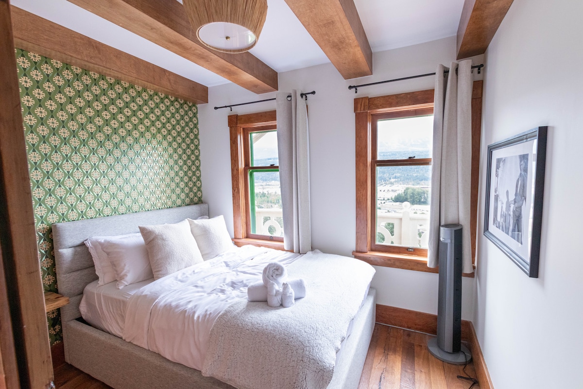 Тази очарователна спалня разполага с открити дървени греди и уникален дизайн на ретро тапети. Големите прозорци позволяват да влезе много естествена светлина, като предлагат спокойно пространство за отдих.