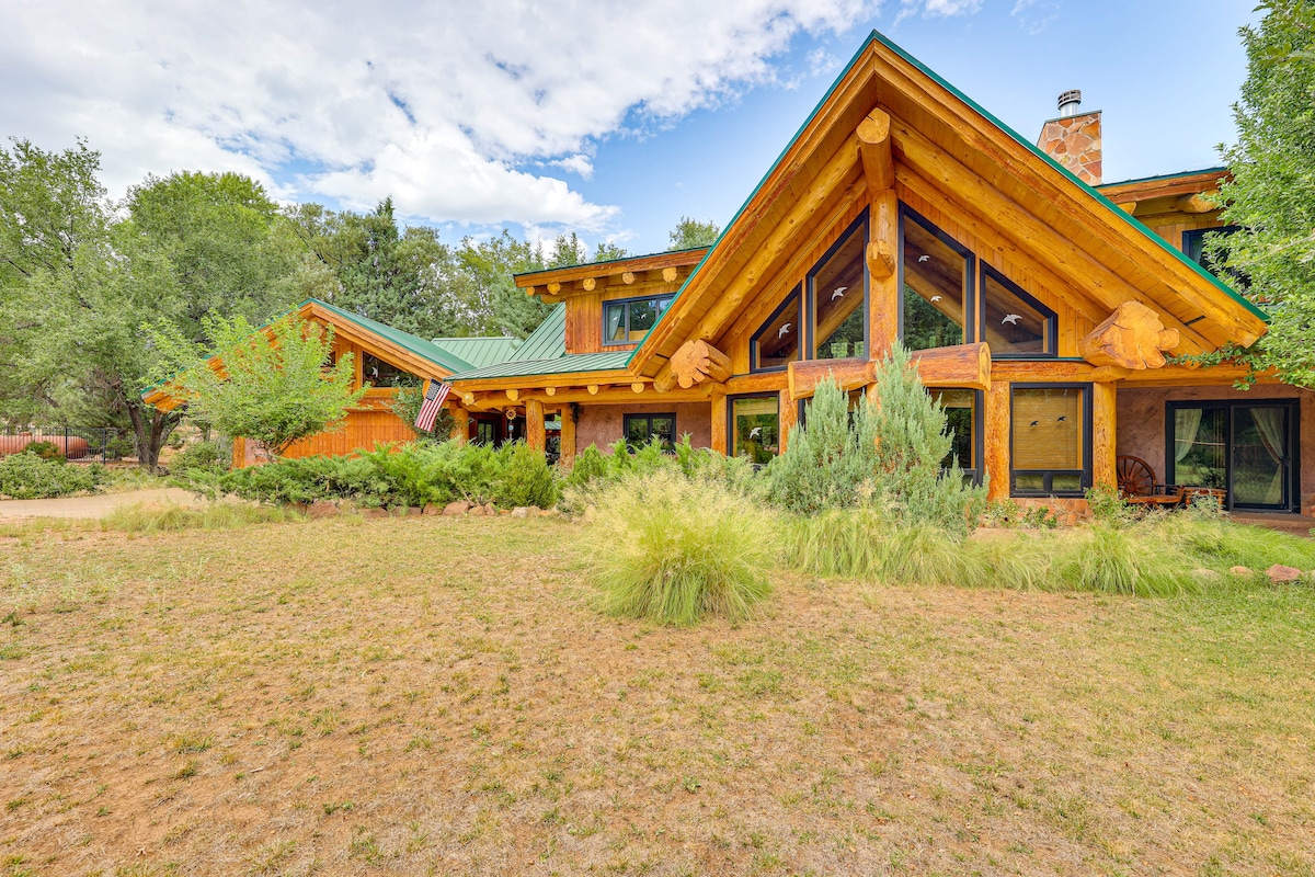 A spacious cabin is nestled among lush greenery, showcasing a distinctive log design with a bright green roof. Large windows allow natural light to fill the interior, while a blend of trees and shrubs surrounds the property, creating a serene outdoor setting.