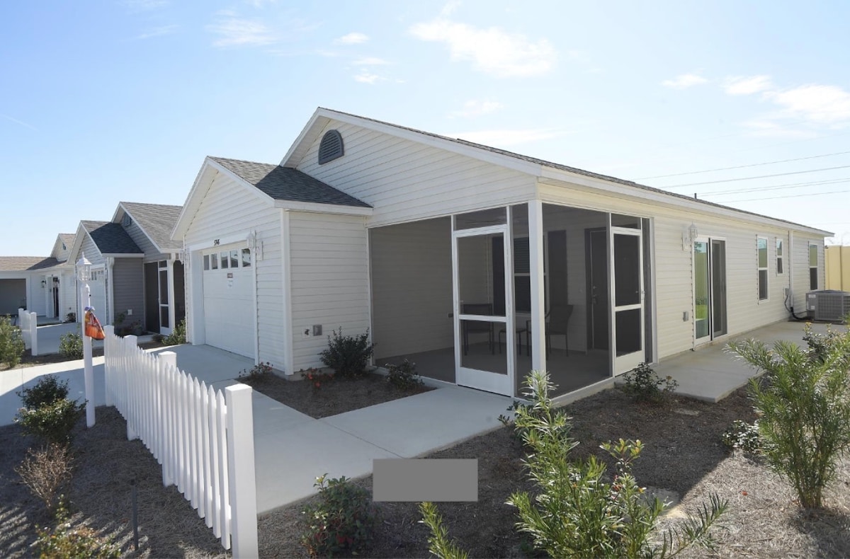 The exterior of the Vibrant Hawkins Villa is captured under a clear blue sky, highlighting a charming single-story structure with light-colored siding. A screened-in lanai is visible, framed by lush greenery, and a white picket fence adds a touch of welcoming charm.