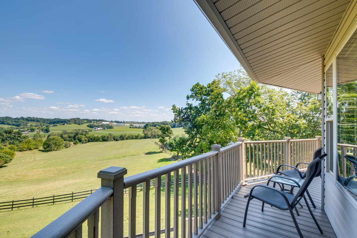 A private wraparound deck offers seating areas with black lounge chairs, overlooking expansive green countryside and rolling hills under a clear blue sky. The natural landscape is framed by tree coverage, creating a serene outdoor setting.