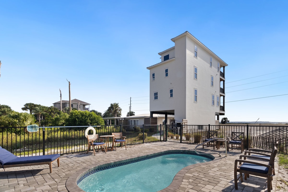 An outdoor space is highlighted by a private, heated pool surrounded by a paver patio. Lounge chairs are positioned for relaxation, with views of the lush landscape beyond. A safety fence encloses the area, enhancing privacy while providing a sense of openness towards the surroundings.