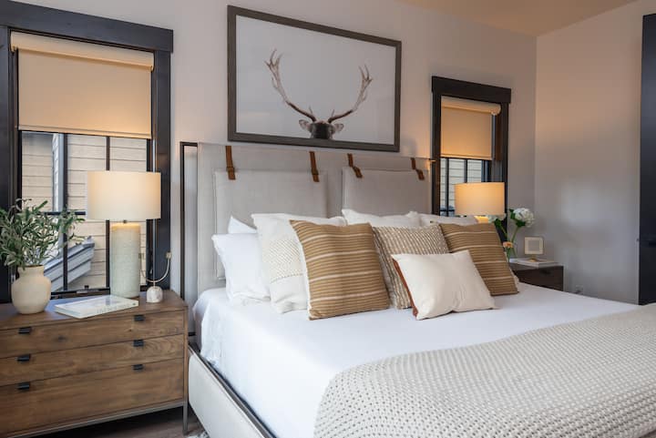 - Подредените една върху друга възглавници и текстурираните одеяла правят тази спалня уютно място за отдих
- Изкуството с рога в рустикален шик и дървени акценти съчетава природата с комфорта
- Мекото осветление и неутралните тонове създават идеалното място за отдих