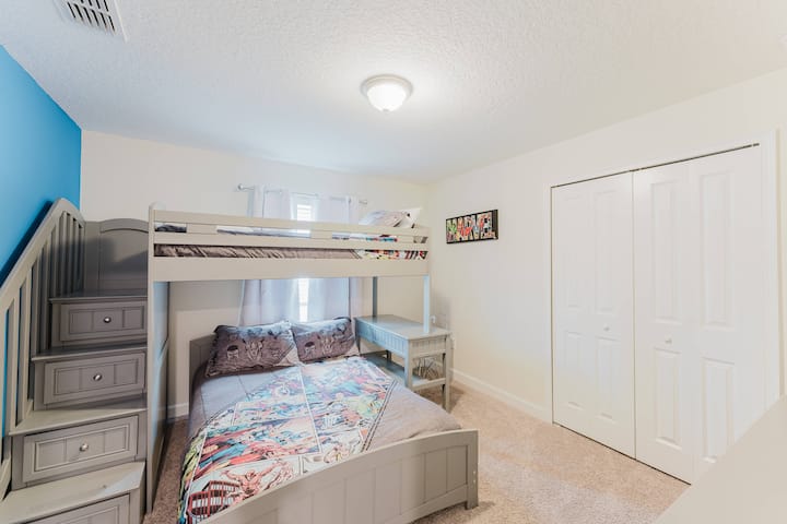 Táto útulná spálňa má veselú poschodovú posteľ ideálnu pre deti alebo hostí. Mäkký béžový koberec a žiarivá modrá stena vytvárajú vyváženú atmosféru, ktorú umocňuje prirodzené svetlo a vytvára tak teplý a príjemný priestor.