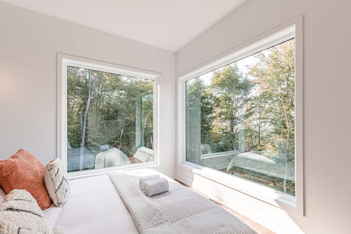 Habitación serena con ventanas de esquina dobles que ofrecen vistas panorámicas al bosque y luz natural.