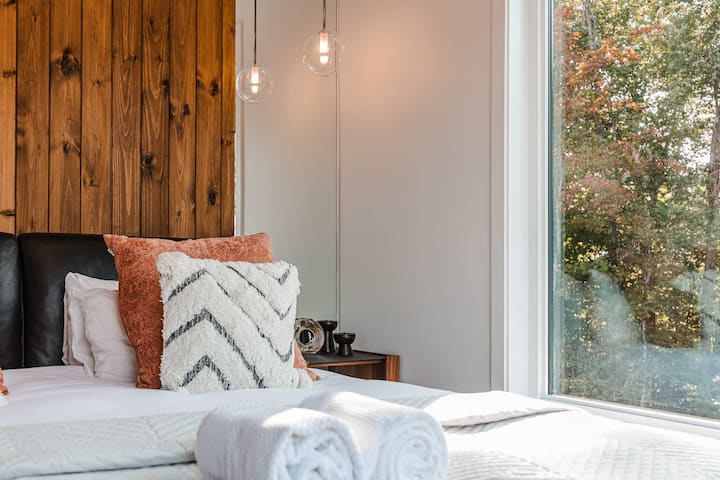 Rincón acogedor de la habitación con almohadas texturizadas, pared decorativa de madera y vista a la ventana grande.