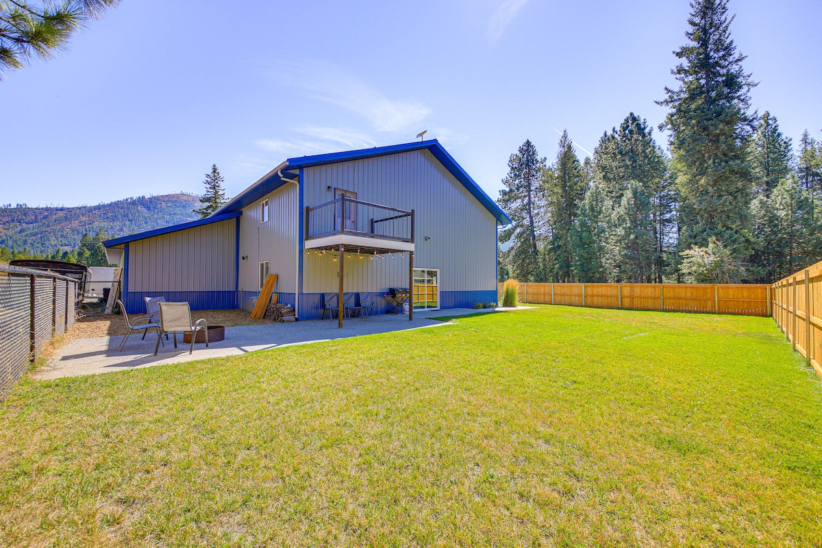 A spacious fenced yard is surrounded by tall trees, with a grassy area that extends towards the horizon. A deck overlooks the yard, providing an outdoor space for relaxation. The exterior of the building features a blue and grey color scheme, complementing the natural scenery.