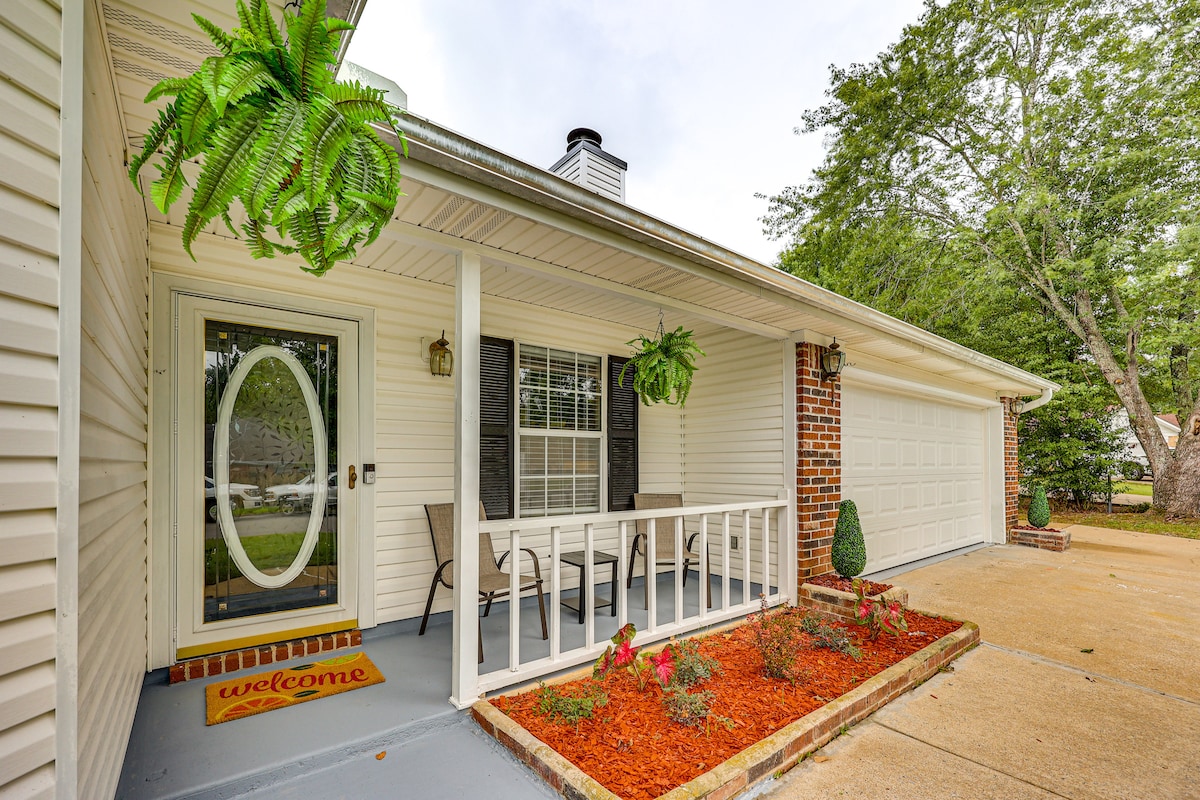 The entrance of the home features a welcoming porch, adorned with potted ferns and a seated area for relaxation. A decorative welcome mat is positioned at the front door, which is framed by two windows, providing natural light to the entryway.