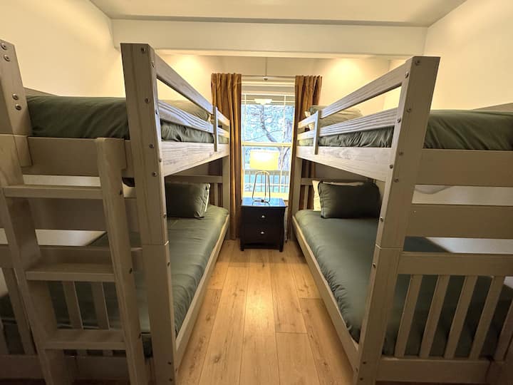 Maliwanag na kuwartong may bunk bed na kayang tumanggap ng 4 na tao na may sahig na kahoy at tanawin sa bintana.