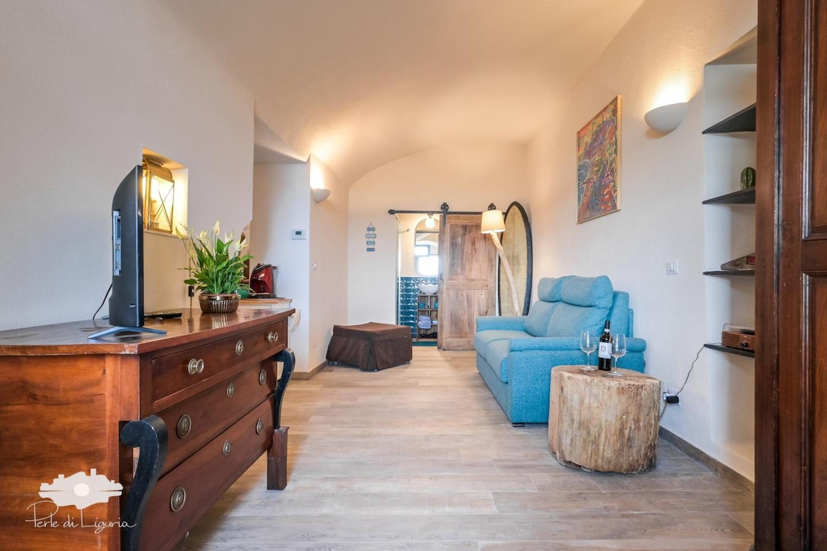 A well-lit living area features a blue sofa and a wooden cabinet with decorative items. A small round table sits near a rustic-style wine rack. Accent lighting provides a warm glow, and artwork adorns the walls, enhancing the room's inviting feel.