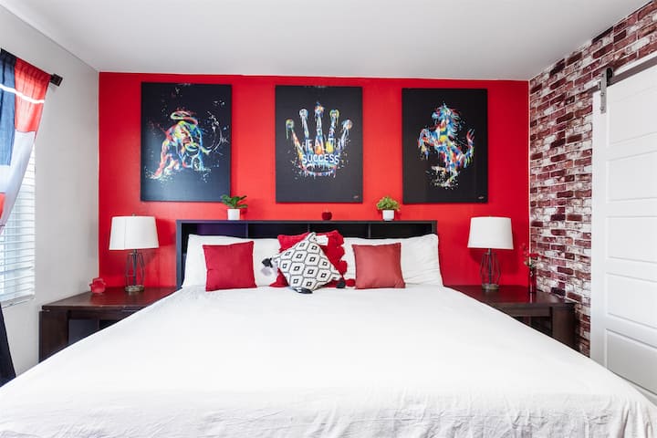 Glavna spavaća soba: mirno utočište udobnosti i stila s luksuznim bračnim krevetom, upečatljivim crvenim ukrasnim zidovima i zadivljujućim umjetničkim djelima koja spajaju kreativnost s opuštanjem.