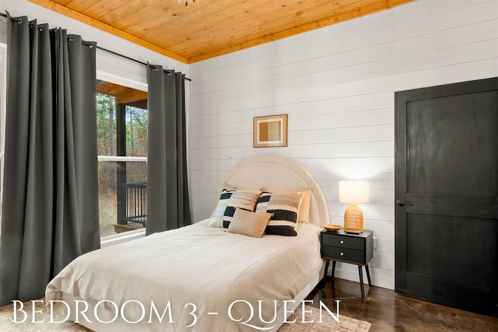 Დედოფლის ზომის მომხიბლავი საწოლი, რომელიც ჩარჩოშია მოქცეული დიდი ფანჯრებით, საიდანაც ბუნებრივი სინათლე იშლება და ღია ცის ქვეშ მშვიდი ხედები იშლება.