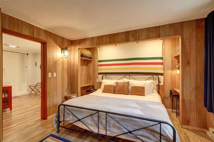 Cama king en el dormitorio 1 con un tema de Pendleton. Reloj despertador y cargadores USB en ambos lados de la cama.