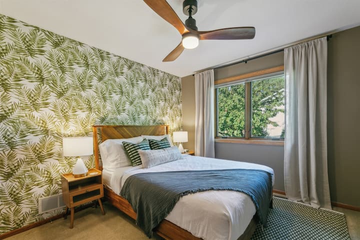The "jungle" bedroom features a queen-sized bed with a new luxury mattress, alarm clock with multiple charging ports, sound machine, and ceiling fan.