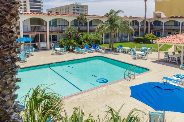 The heated swimming pool is surrounded by spacious areas for lounging. Poolside chairs and tables are arranged for relaxation, and the courtyard features well-maintained greenery and a gazebo. Umbrellas provide shade for outdoor comfort, creating a welcoming environment for guests.